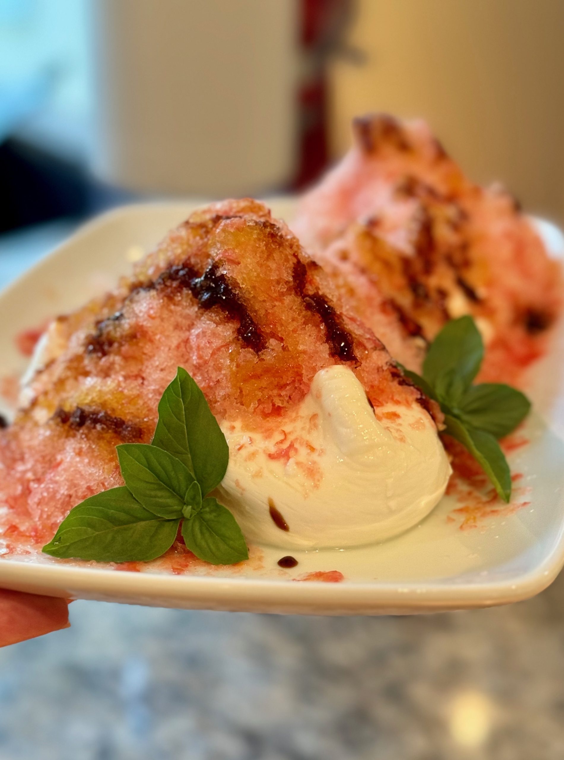 Burrata cheese topped with tomato shave ice and drizzled with balsamic glaze, olive oil and flaky salt. Garnished with sprigs of basil.