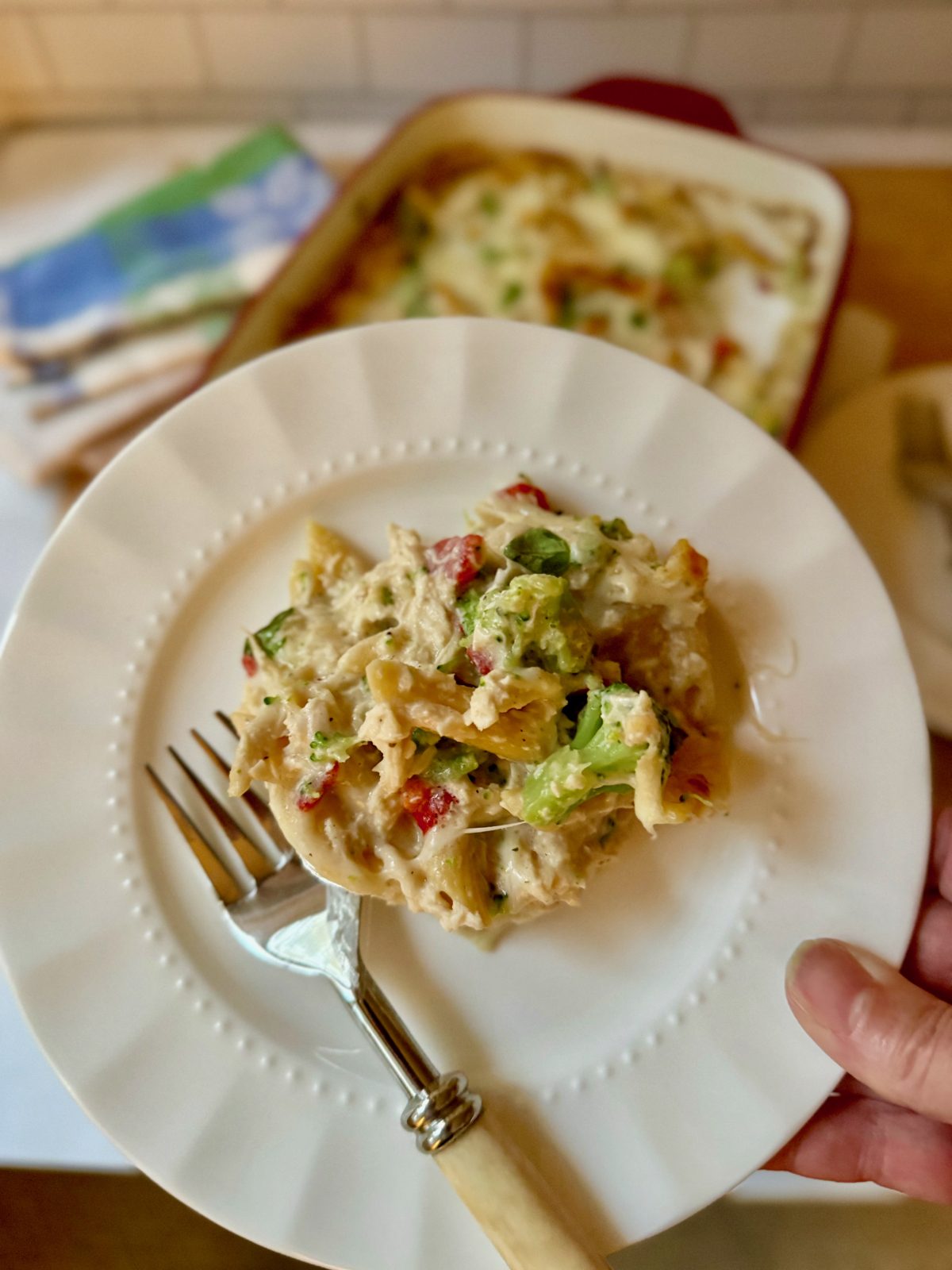 Plate with one serving of chicken and broccoli pasta bake, faded in distance is casserole dish.