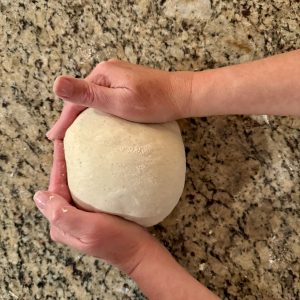 2 hands shaping some sourdough dough on a granite countertop