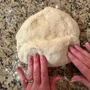 2 hands shaping some sourdough dough on a granite countertop