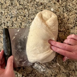 2 hands shaping some sourdough dough on a granite countertop