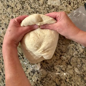 2 hands shaping some sourdough dough on a granite countertop