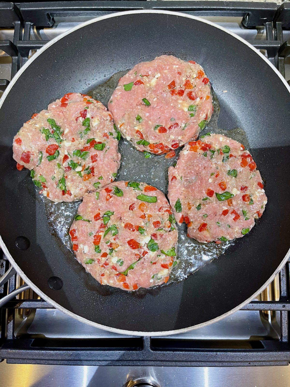 4 uncooked turkey burger patties in a black non-stick skillet