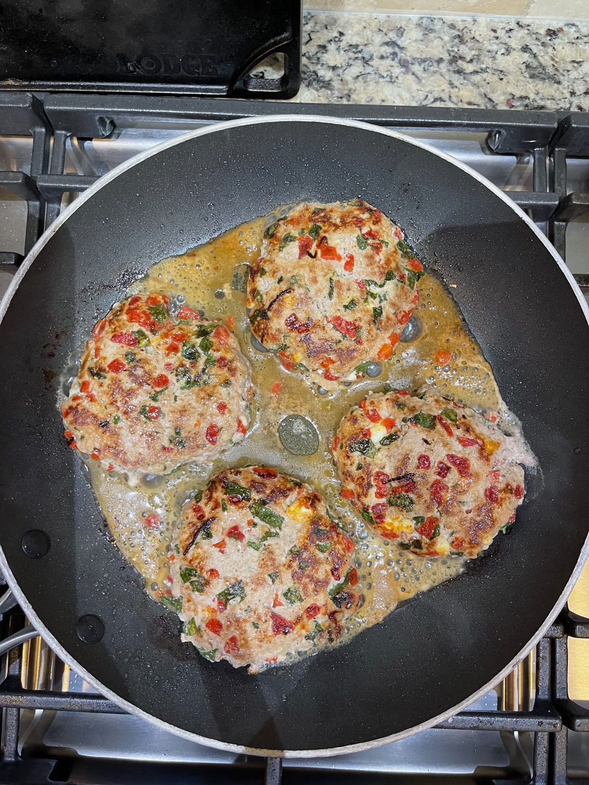 4 Turkey Burgers almost done cooking in a black non-stick skillet.