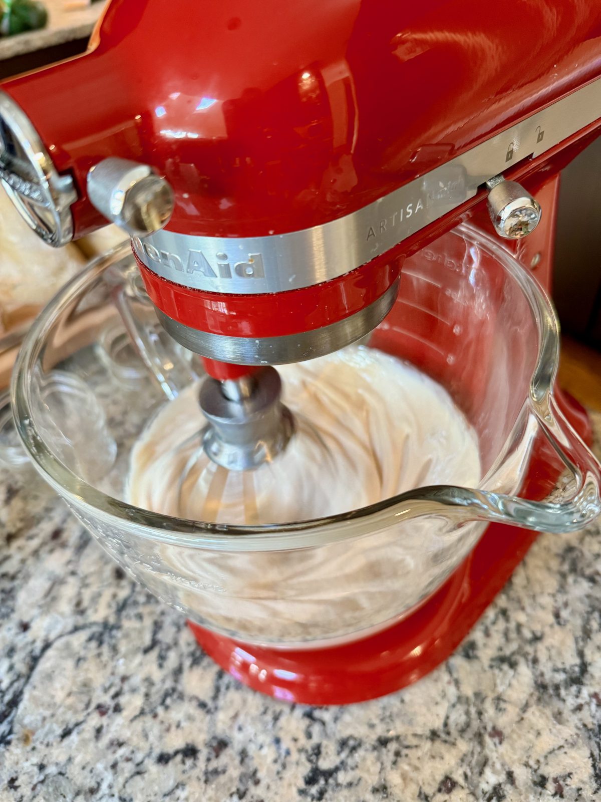 Red KitchenAid Stand Mixer with Glass Bowl and whip beater accessory.  Whipping honey in the bowl.