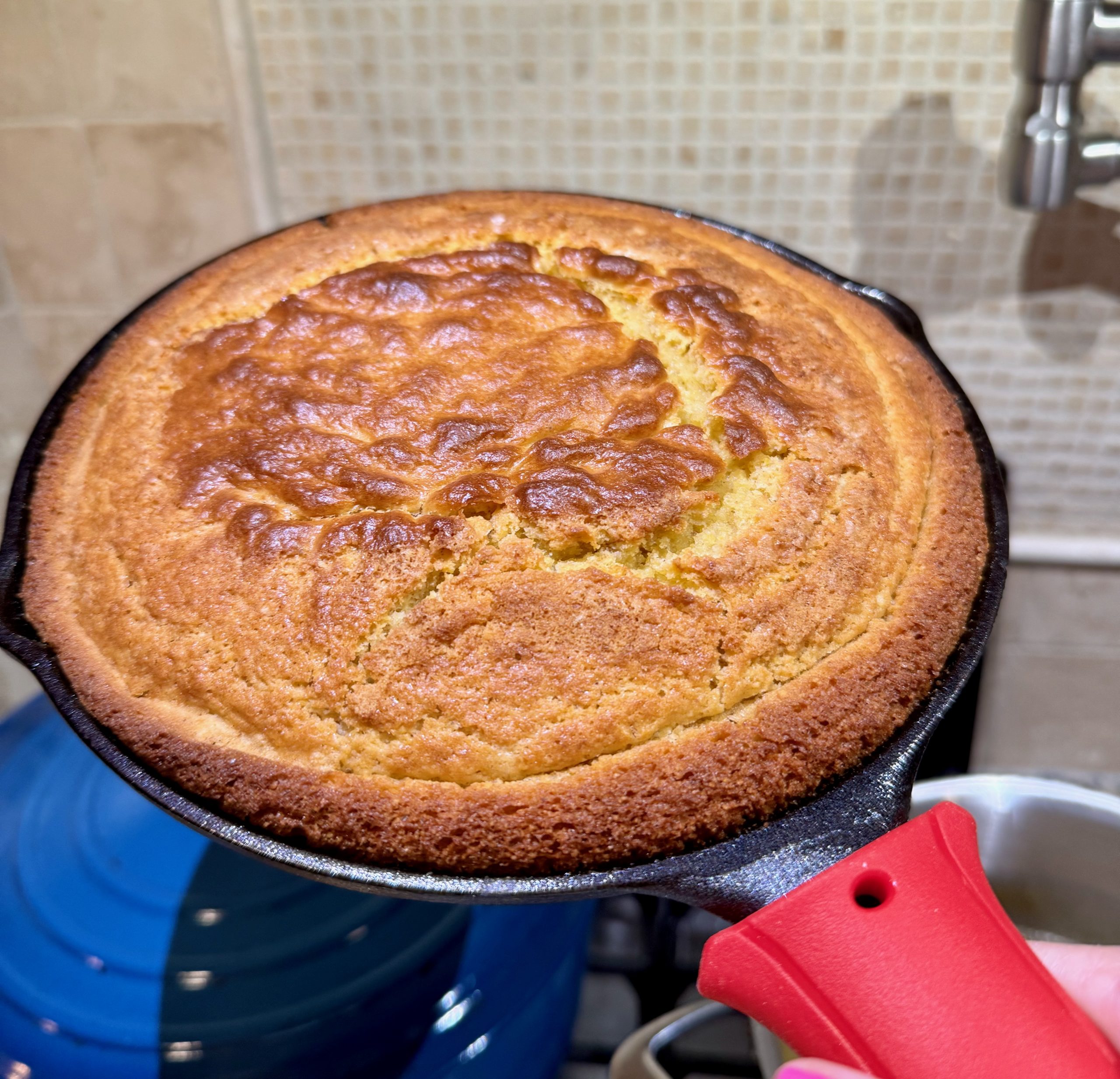 Recipe Photo showing golden brown baked sourdough cornbread in 8 inch cast iron skillet with red heat protector on handle.