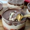 4 Clear glass cups with layered Greek Yogurt treat. Strawberry jam on the bottom, peanut butter yogurt mixture in the middle and magic chocolate shell on top. sprinkled with flaky salt and a spoon breaking through the chocolate.