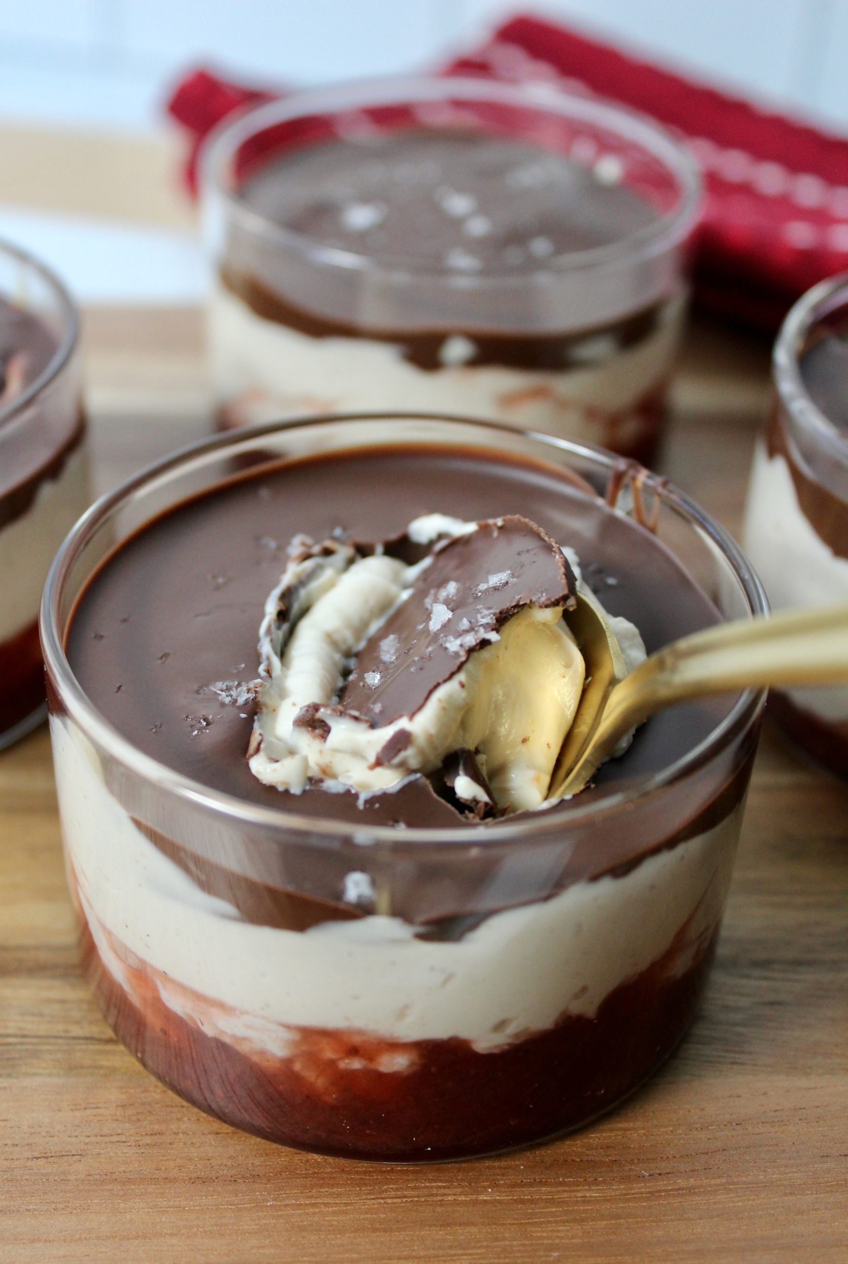 4 Clear glass cups with layered Greek Yogurt treat. Strawberry jam on the bottom, peanut butter yogurt mixture in the middle and magic chocolate shell on top. sprinkled with flaky salt and a spoon breaking through the chocolate.